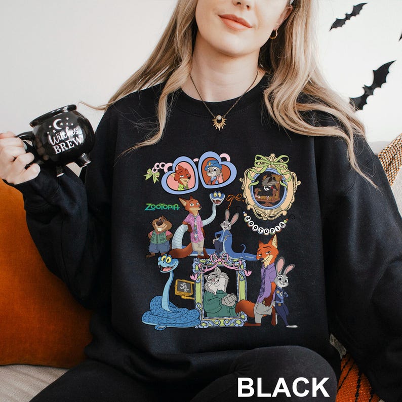 May include: Black sweatshirt with a colourful graphic of characters from the animated film Zootopia. The design includes images of Nick Wilde, Judy Hopps, and other characters. The word "Zootopia" is printed in green. The word "BLACK" is printed at the bottom.
