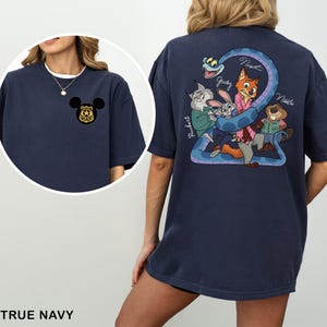 May include: True navy blue t-shirt with a Mickey Mouse police badge on the front and a Zootopia-themed graphic on the back. The back graphic features characters like Judy, Nick, and others, with a blue snake forming the number 2.