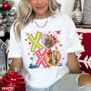 May include: White t-shirt featuring a colorful graphic design with the characters from Zootopia. The design includes the letters "XO", hearts, and images of Judy Hopps and Nick Wilde. The word "WHITE" is printed at the bottom.