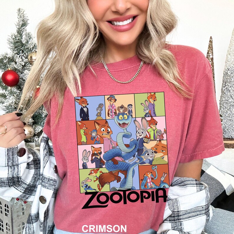 May include: Crimson-colored t-shirt featuring a colorful graphic of characters from the animated movie "Zootopia." The design includes a snake, fox, and rabbit, with the word "Zootopia" in bold black letters. The shirt is a short-sleeved crew neck.