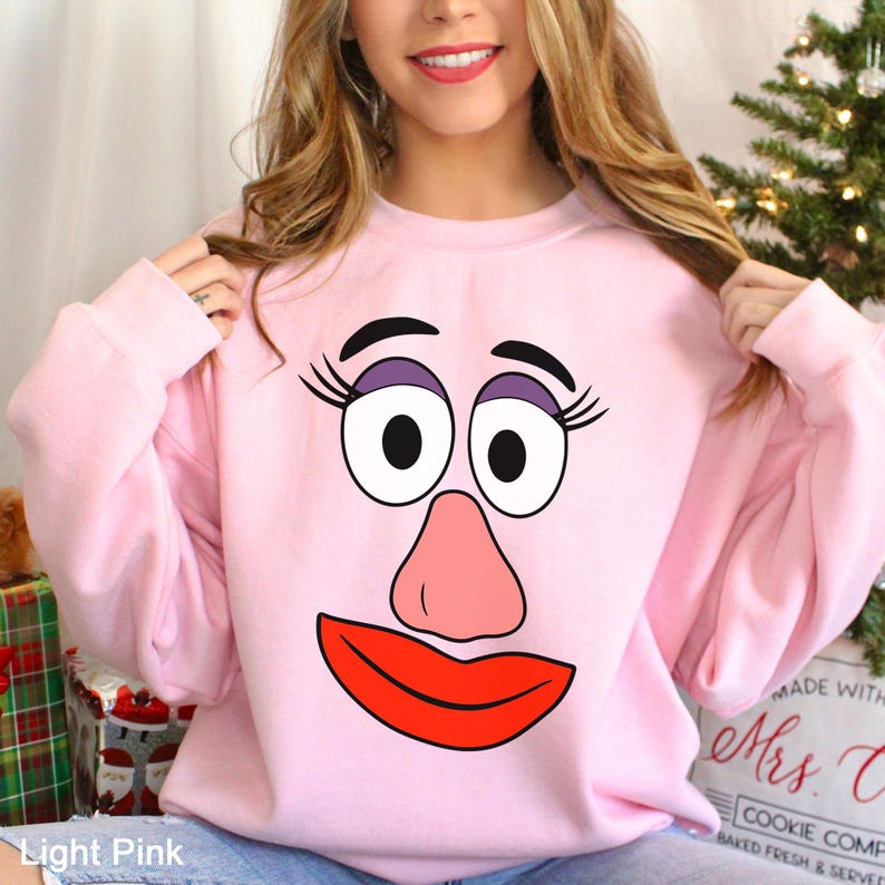 May include: Light pink sweatshirt featuring a cartoon face with large eyes, eyelashes, a nose, and red lips. The sweatshirt is a solid light pink color. The text "Light Pink" is at the bottom left of the image.