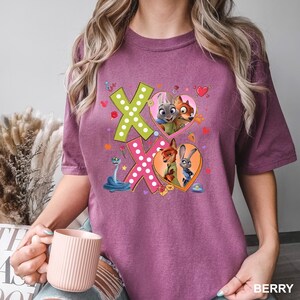 May include: Berry-colored t-shirt featuring the characters from Zootopia. The design includes the letters "XO" with heart-shaped images of the characters. A blue snake and other small graphics are also included in the design.