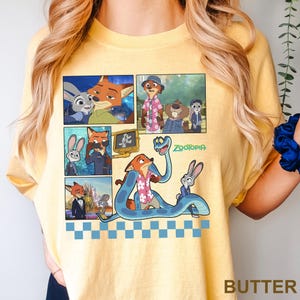 以下が含まれることがあります： アニメ映画「ズートピア」のキャラクターが描かれたコミックストリップデザインのイエローTシャツ。キツネ、ウサギ、その他のキャラクターの画像が含まれています。「ズートピア」の文字は緑色で印刷されています。