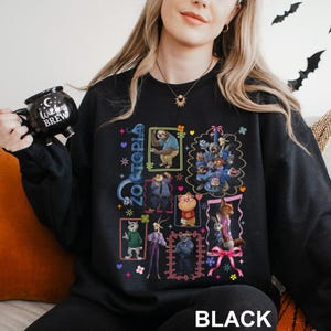 Puede incluir: Sudadera negra de Zootopia con ilustraciones coloridas de personajes en cuadros enmarcados. La palabra "Zootopia" est&aacute; escrita verticalmente en azul. La palabra "BLACK" est&aacute; impresa en blanco en la parte inferior de la sudadera.