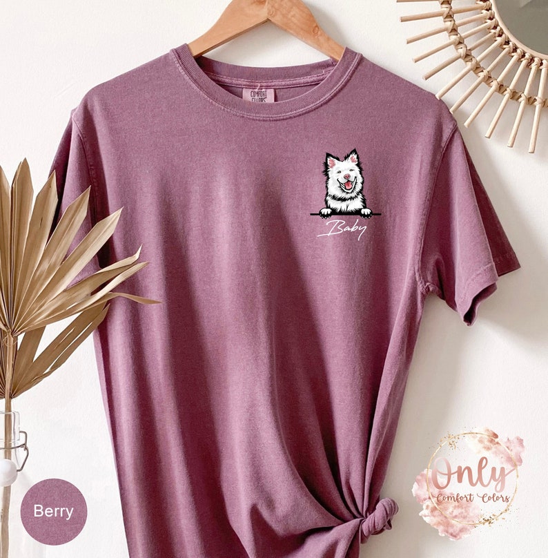 May include: A mauve t-shirt with a white dog peeking over the top and the word "Baby" written below.