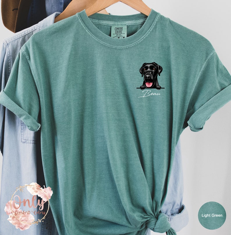 May include: Light green t-shirt with a black Labrador Retriever peeking over the top of a pocket. The dog's name, "Bear", is written in cursive below the dog.