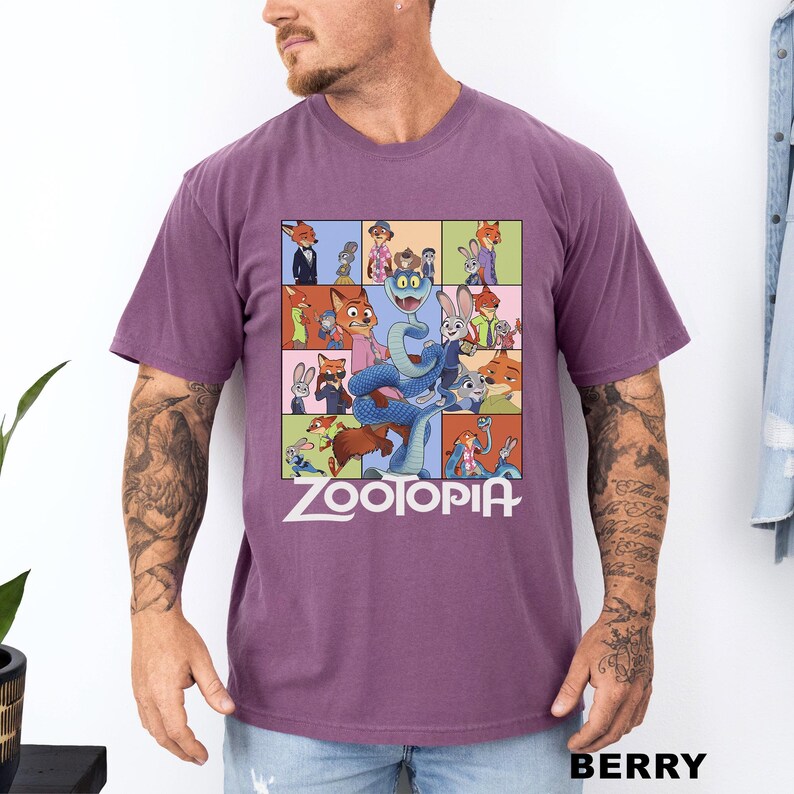 May include: Berry-colored t-shirt featuring a colorful graphic from the animated movie Zootopia. The design includes various characters from the film, with the word "Zootopia" in white block letters at the bottom. The shirt has short sleeves.