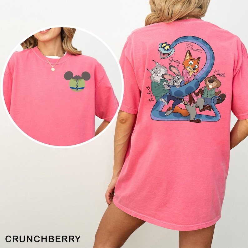 May include: A pink t-shirt with a cartoon design on the front and back. The front has a Mickey Mouse head with a tie. The back has a blue snake with cartoon characters and the names Judy, Nick, and Nibbles. The word "Crunchberry" is at the bottom.