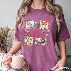 May include: Berry-colored t-shirt featuring a graphic with four framed cartoon characters and the text "HAPPY VALENTINE'S DAY." The characters include a rabbit, fox, cheetah, and a bull, each with Valentine's Day-themed elements like hearts and gifts.