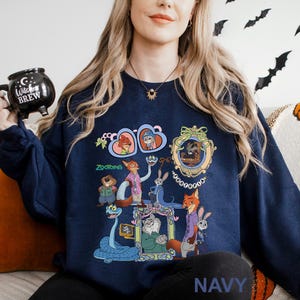 May include: Navy blue sweatshirt with a colourful graphic of characters from the animated film "Zootopia." The design includes various animal characters in ornate frames and the word "Zootopia." The sweatshirt also has the word "NAVY" printed at the bottom.