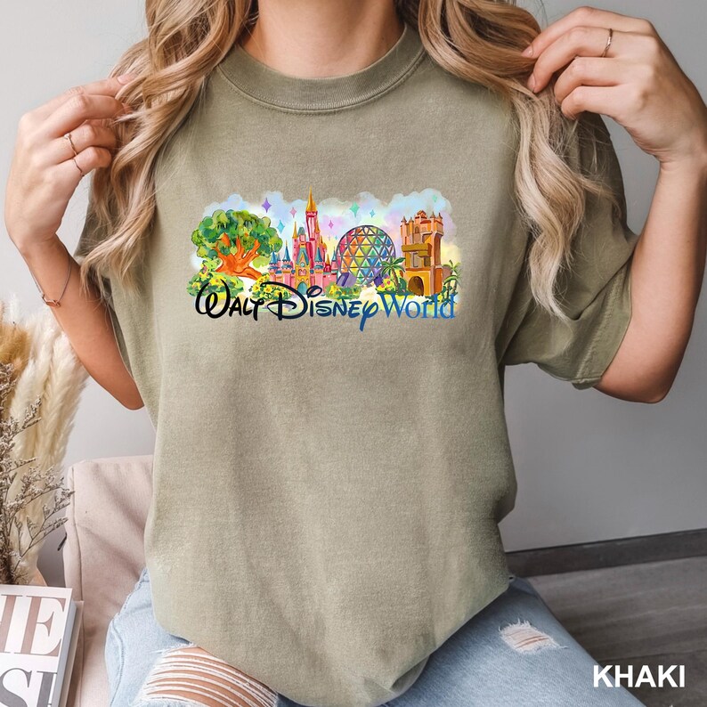 K&ouml;nnte beinhalten: Ein khakifarbenes T-Shirt mit Rundhalsausschnitt und einem farbenfrohen Grafikdruck der Walt Disney World Skyline, einschlie&szlig;lich des Tree of Life, Cinderella Castle, Spaceship Earth und Tower of Terror, mit dem Schriftzug Walt Disney World.