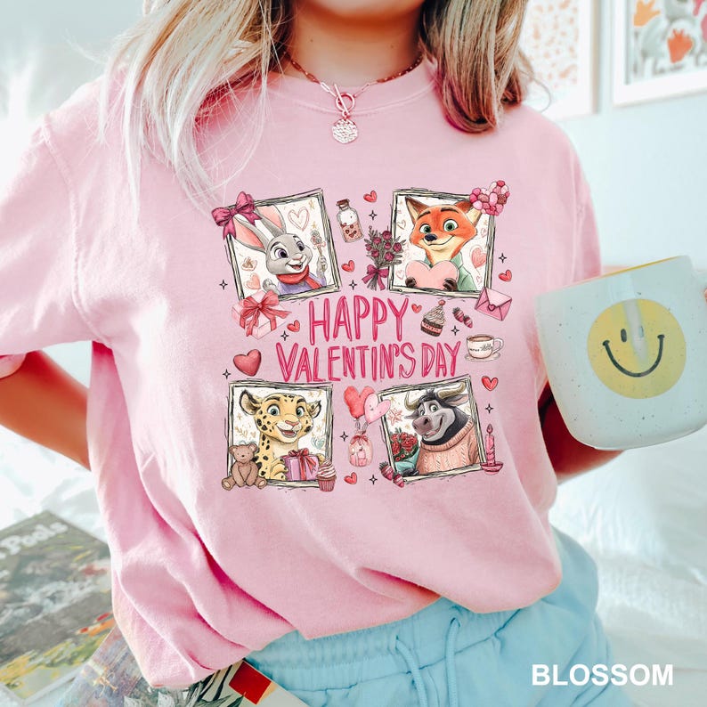 May include: Pink t-shirt with a Valentine's Day graphic featuring cartoon characters and the text "Happy Valentine's Day." The shirt also has a white mug with a yellow smiley face. The word "BLOSSOM" is at the bottom.