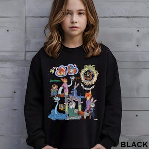 May include: Black sweatshirt with a colourful graphic of characters from the animated film "Zootopia." The design includes various animal characters in ornate frames and the movie title. The word "BLACK" is printed at the bottom right.