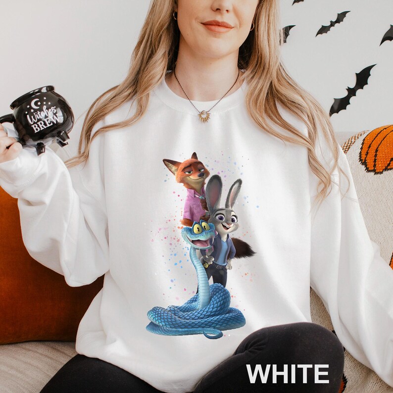 K&ouml;nnte beinhalten: Wei&szlig;es Sweatshirt mit einem farbenfrohen Aufdruck von Charakteren aus dem Animationsfilm Zootopia. Das Design zeigt einen Fuchs, ein Kaninchen und eine Schlange. Das Wort "WHITE" ist unten auf dem Sweatshirt in gro&szlig;en Buchstaben aufgedruckt.