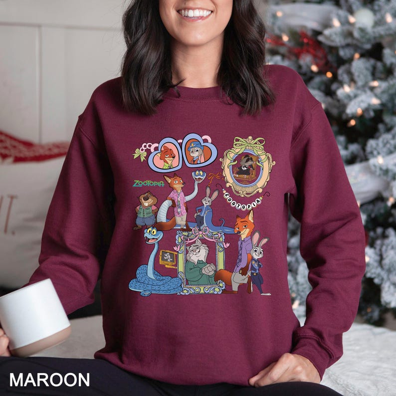 May include: Maroon sweatshirt with a colourful graphic of Zootopia characters. The design includes various characters in ornate frames and decorative elements. The word "Zootopia" is also printed on the sweatshirt.