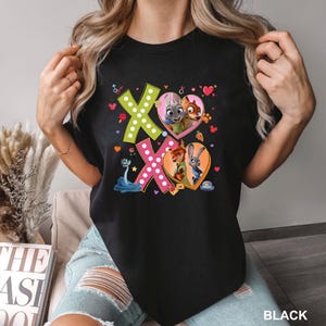 May include: Black t-shirt featuring the characters from Zootopia. The design includes the letters "XO" in green and pink, with heart-shaped illustrations of the characters. The word "BLACK" is printed at the bottom right.