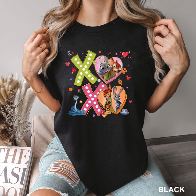 May include: Black t-shirt featuring the characters from Zootopia. The design includes the letters "XO" in green and pink, with heart-shaped illustrations of the characters. The word "BLACK" is printed at the bottom right.