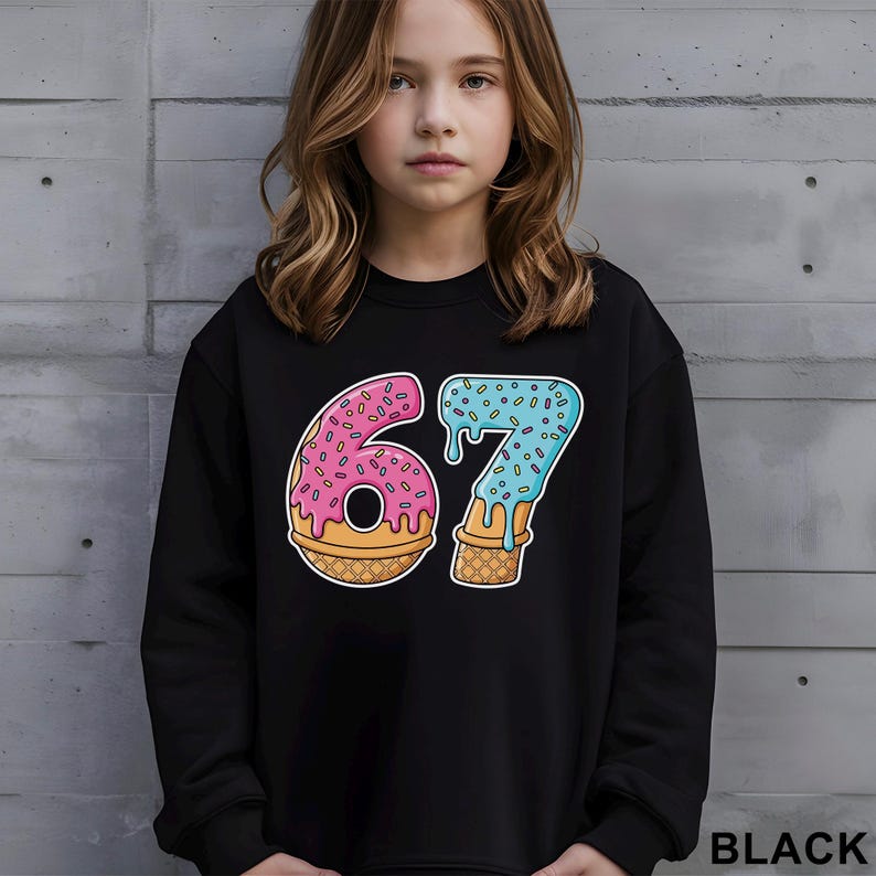 May include: Black sweatshirt with a colorful graphic of the number 67 designed as a donut and ice cream cone. The number 6 is pink with sprinkles, and the 7 is blue with sprinkles. The word "BLACK" is printed in white at the bottom right.