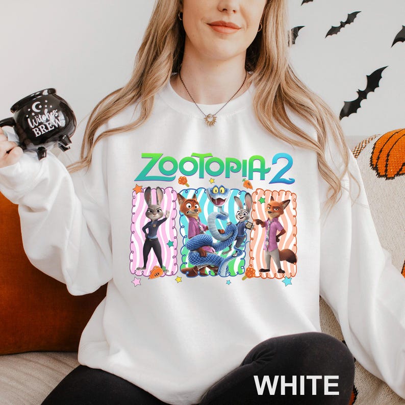 Puede incluir: Sudadera blanca con el texto "ZOOTOPIA 2" y un gr&aacute;fico colorido de personajes de la pel&iacute;cula animada. El gr&aacute;fico incluye a Judy Hopps, Nick Wilde y otros personajes. La palabra "WHITE" est&aacute; impresa en la parte inferior.