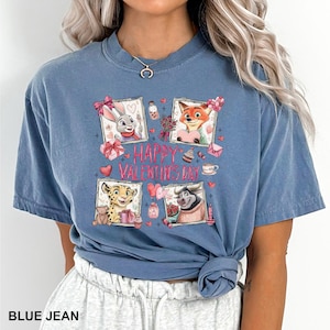 May include: Blue jean colored t-shirt featuring a Valentine's Day design. The design includes four framed images of cartoon animals, hearts, gifts, and the text "HAPPY VALENTINE'S DAY". The shirt is a short-sleeved, crew neck style.