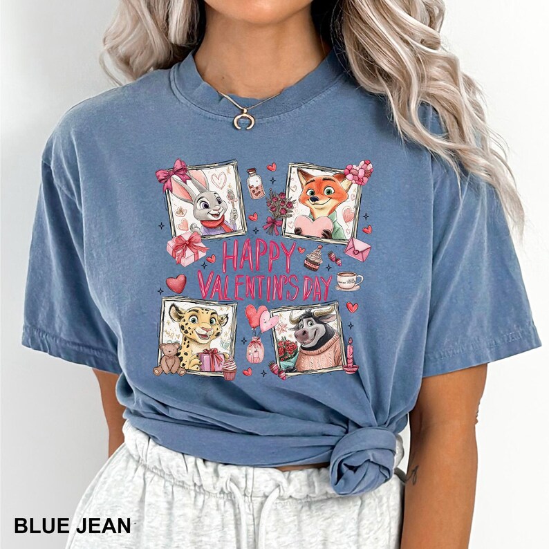 May include: Blue jean colored t-shirt featuring a Valentine's Day design. The design includes four framed images of cartoon animals, hearts, gifts, and the text "HAPPY VALENTINE'S DAY". The shirt is a short-sleeved, crew neck style.