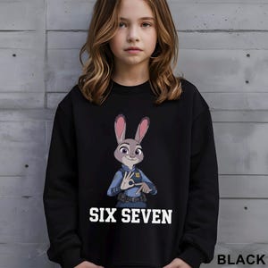 May include: Black sweatshirt featuring a cartoon image of Judy Hopps from Zootopia, in a police uniform, with the text "SIX SEVEN" in white. The word "BLACK" is printed in the lower right corner. The sweatshirt is worn by a young person.