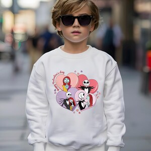 May include: White sweatshirt featuring a graphic of characters from The Nightmare Before Christmas inside heart shapes. The phrase "Happy Valentine's Day" is printed on the left side. The design includes Jack Skellington, Sally, and other characters.