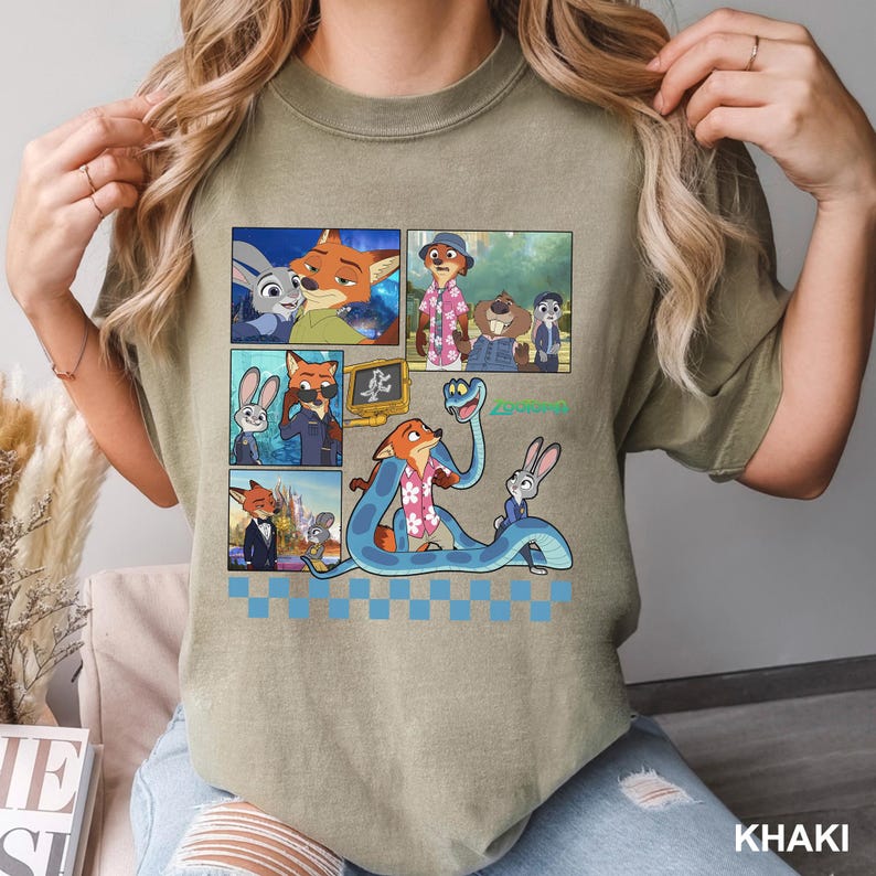 以下が含まれることがあります： カーキ色のTシャツ。アニメ映画「ズートピア」のキャラクターのカラフルなグラフィックが特徴です。デザインには、キャラクターの画像が複数パネルで表示され、緑色のスクリプトで「Zootopia」の文字が描かれています。