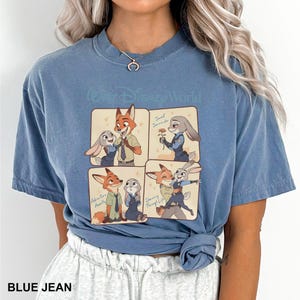 K&ouml;nnte beinhalten: Ein kurz&auml;rmeliges T-Shirt in Jeansblau mit einer vierteiligen Grafik von Nick Wilde und Judy Hopps aus Zoomania. Der Text lautet Walt Disney World, Sweet Surrender, Adventure Awaits und Dancing Through Life in einem Cartoon-Stil.