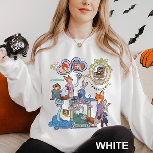 May include: White sweatshirt with a colourful graphic of characters from the animated film "Zootopia." The design features cartoon animal characters, with the word "Zootopia" displayed. The sweatshirt is a casual, long-sleeved garment, suitable for everyday wear.