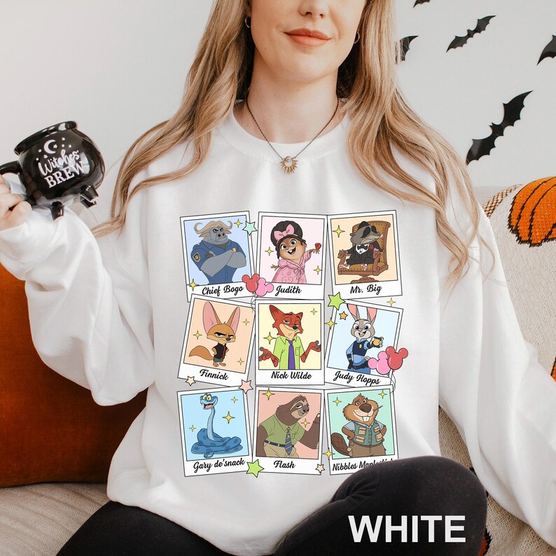 Puede incluir: Sudadera blanca con retratos de personajes de dibujos animados en marcos de Polaroid. Los personajes incluyen a Chief Bogo, Judy Hopps, Nick Wilde y otros. La palabra "WHITE" est&aacute; impresa en la parte inferior.