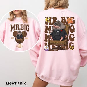 K&ouml;nnte beinhalten: Hellrosa Sweatshirt mit einer Cartoon-Illustration eines Charakters im Anzug, der in einem Stuhl sitzt. Auf der Vorderseite steht "MR. BIG", auf der R&uuml;ckseite wiederholen sich Text und Illustration. Der Text "Zootopia 2" ist ebenfalls sichtbar.