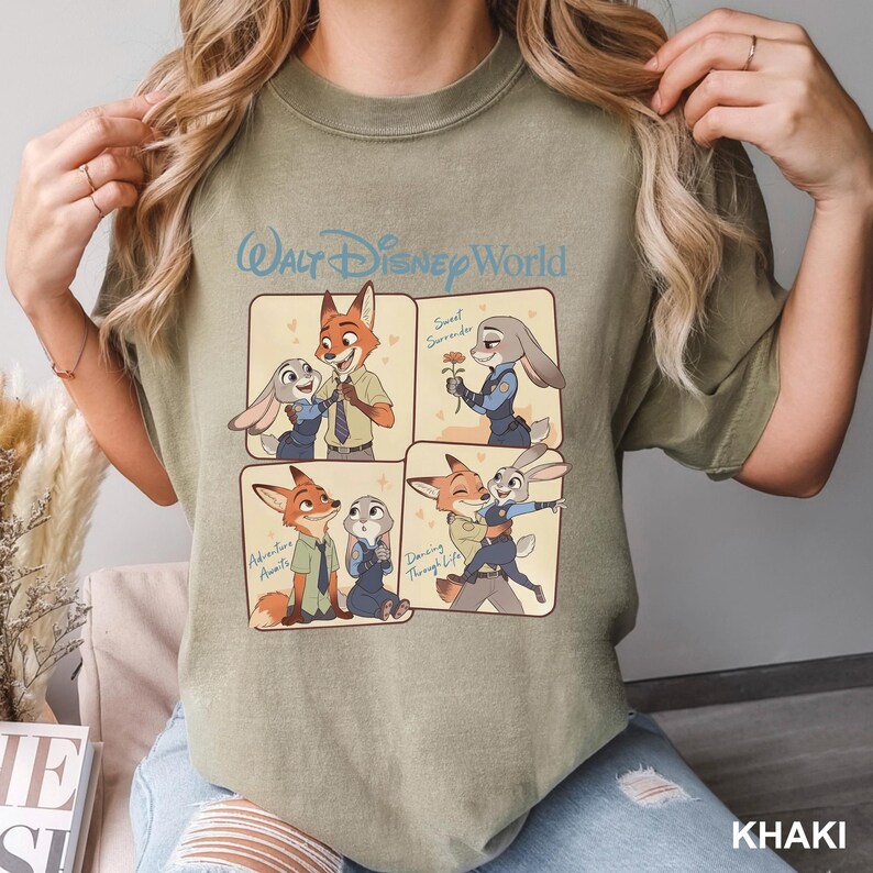 K&ouml;nnte beinhalten: Ein khakifarbenes T-Shirt mit Rundhalsausschnitt und einem Walt Disney World-Grafikdruck, der in vier Feldern die Zeichentrickfiguren Nick Wilde und Judy Hopps in verschiedenen Szenen zeigt, inklusive der Texte Sweet Surrender, Adventure Awaits und Dancing Through Life.