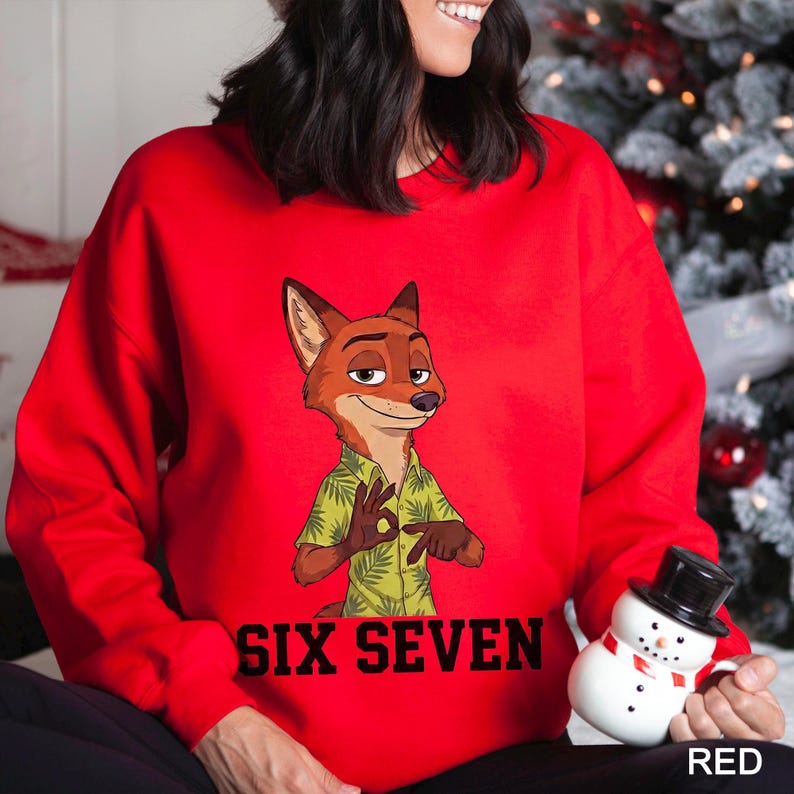 May include: A red sweatshirt featuring a cartoon fox character in a green shirt with a leaf pattern. The text "SIX SEVEN" is printed in black below the fox. A small snowman figurine is visible on the right.