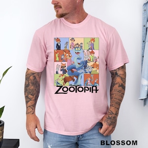 May include: Light pink t-shirt featuring a colorful graphic from the animated movie Zootopia. The design includes various animal characters in a grid pattern, with the movie title in black at the bottom. The shirt is short-sleeved.