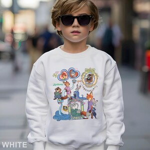May include: White sweatshirt with a colourful graphic of characters from the animated film "Zootopia." The design includes various animal characters in detailed illustrations. The word "Zootopia" is also printed on the sweatshirt.