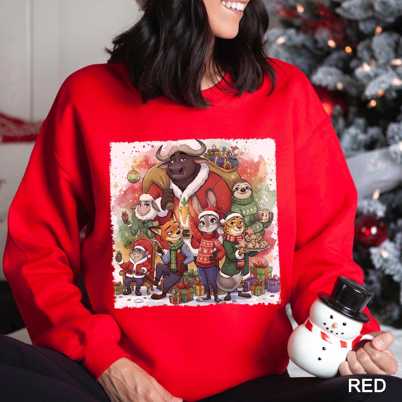Op de afbeelding: Een rode sweatshirt met een feestelijke illustratie van verschillende dierenfiguren in een winterse sc&egrave;ne. Het ontwerp bevat een stier, een konijn, een vos en andere dieren, allemaal gekleed in feestelijke kleding. Het woord "RED" staat onderaan.