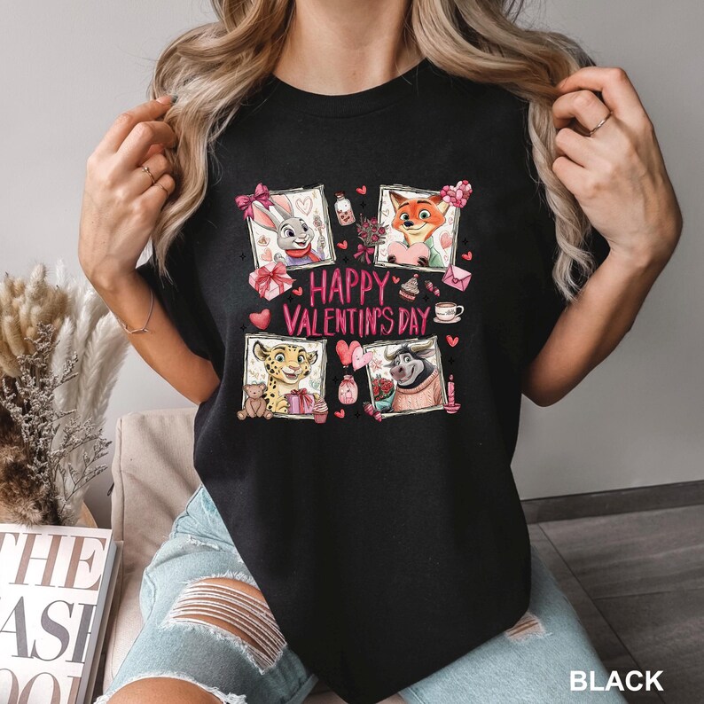 May include: Black t-shirt featuring four framed cartoon characters with Valentine's Day themed elements. The words "HAPPY VALENTINE'S DAY" are in pink. The shirt is made of a soft material.