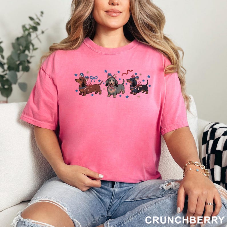 Peut inclure: T-shirt rose avec trois teckels orn&eacute;s de n&oelig;uds patriotiques et d'&eacute;toiles. Le mot "CRUNCHBERRY" est imprim&eacute; en bas. Le t-shirt est de style d&eacute;contract&eacute;.