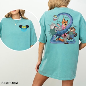 May include: Seafoam green t-shirt with a cartoon character on the front and a group of cartoon characters on the back. The back of the shirt has a large number 2 with cartoon characters. The shirt is made of a soft, comfortable material.