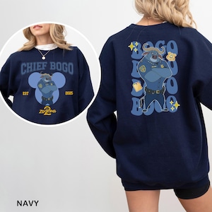 K&ouml;nnte beinhalten: Marineblaues Sweatshirt mit Chief Bogo aus Zootopia. Auf der Vorderseite steht "CHIEF BOGO" und ein Cartoon-Bild von Chief Bogo. Auf der R&uuml;ckseite befindet sich eine gr&ouml;&szlig;ere Grafik von Chief Bogo mit Text und Sternen. Das Wort "NAVY" steht unten.