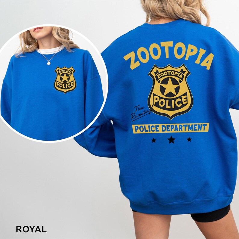 Puede incluir: Sudadera azul real con una insignia del Departamento de Polic&iacute;a de Zootopia en la parte delantera y trasera. La parte trasera de la sudadera muestra la palabra "Zootopia" en amarillo, junto con la insignia de la polic&iacute;a y el texto "Police Department".