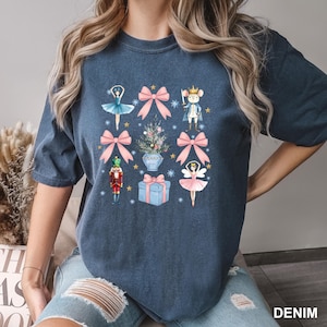 May include: Denim blue t-shirt featuring a grid of watercolor illustrations. The design includes ballerinas, bows, a Christmas tree, a nutcracker, a gift box, and a mouse king. The word "DENIM" is printed in white at the bottom right.