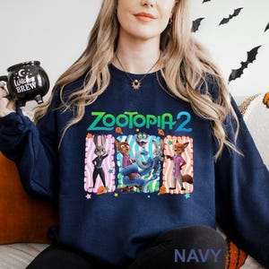 Puede incluir: Sudadera azul marino con el texto "ZOOTOPIA 2" y personajes de dibujos animados. El dise&ntilde;o incluye un conejo, un zorro y otros personajes en marcos rectangulares coloridos. La palabra "NAVY" est&aacute; impresa en la parte inferior.