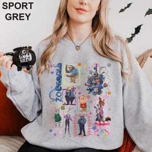Puede incluir: Sudadera gris deportiva con un gr&aacute;fico colorido de personajes de Zootopia. El dise&ntilde;o incluye la palabra "Zootopia" en una fuente estilizada, junto con varios personajes de animales en cuadros enmarcados. La sudadera es de color gris claro.