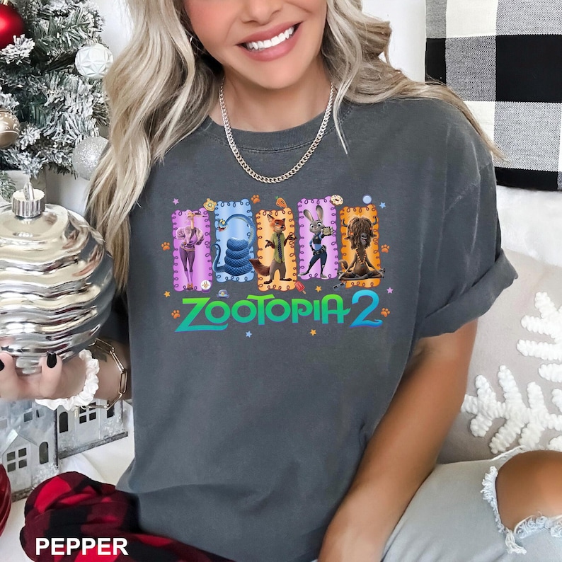 K&ouml;nnte beinhalten: Ein anthrazitfarbenes Kurzarm-T-Shirt mit einem Grafikdruck der Zootopia 2-Figuren in f&uuml;nf bunten rechteckigen Rahmen. Das Design enth&auml;lt den Schriftzug Zootopia 2 in t&uuml;rkiser Schrift, akzentuiert durch kleine orangefarbene Pfotenabdr&uuml;cke und Sterne.
