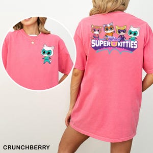 May include: A pink short-sleeve t-shirt featuring a small white Super Kitties character on the front left chest and a large graphic on the back with four Super Kitties characters and the text Disney Junior SUPER KITTIES.