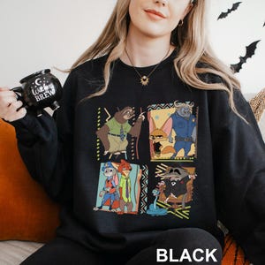 May include: Black sweatshirt featuring a four-panel design with characters from the animated movie Zootopia. The panels include a sloth, a fox, a buffalo, and a raccoon. The word "BLACK" is printed at the bottom.
