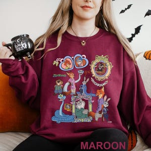 May include: Maroon sweatshirt with a vibrant graphic of Zootopia characters. The design showcases animal characters in frames and the word "Zootopia". The word "MAROON" is printed at the bottom of the sweatshirt.