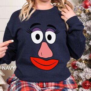 May include: Navy blue sweatshirt featuring a cartoon face with large white eyes, a pink nose, and a red mouth. The word "NAVY" is printed on the bottom left. The sweatshirt is part of a clothing collection.